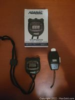 Photo showing new Adanac Marathon stopwatch in original white box and used lap counter side by side on a wooden surface.