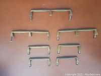 Six vintage brass handles of varying sizes laid out on a flat wooden surface, showing full set of handles.