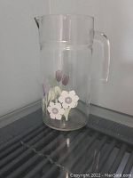 Glass juice pitcher showing floral designs and handle from side angle