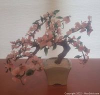 Full view of glass bonsai tree with pink flowers and green leaves in ceramic pot.