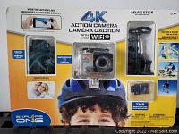 Photo of unopened box of 4K Action Camera with WiFi, showing camera inside waterproof case with accessories including selfie stick, tripod, and 32GB microSD card.