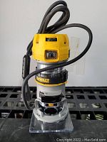 DeWalt compact router with power cord on black surface, showing front controls and base plate