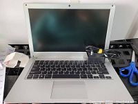 Opened silver notebook laptop with screen, keyboard, touchpad and power adapter placed on black grid surface