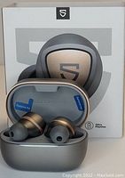 Photo of SoundPEATS Sonic true wireless earbuds displayed in their open charging case with the product box behind them. Earbuds and case have metallic gray and bronze finish with protective film stickers.