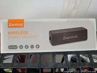 Front side of retail box showing Zamkol Wireless Stereo Speaker Model ZK106 branding and icons for features.