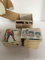 Stacks of 1978-79 O-Pee-Chee hockey cards in front of an original box labeled for the set year and type. Visible cards show player pictures and team data.