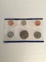 Photo of the first clear plastic sleeve holding six 1991 US Mint proof coins with a blue border, showing various denominations including penny, dime, nickel, quarter, half dollar, and dollar coins.