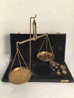 Full view of vintage brass balance scale set up in black fitted case showing two weighing pans and weights on the right side.