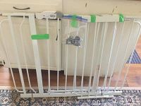 Full view of white metal baby gate leaning against a cabinet, showing the gate's size and structure.