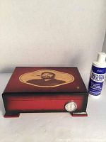 Closed wooden humidor with reddish finish, Che Guevara portrait on lid, and hygrometer on front.