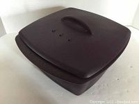 Closed view of the dark brown silicone steamer with lid and handle.