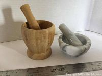 Two mortar and pestle sets side by side with a ruler for scale, showing wood and marble materials.