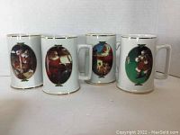Photo showing all four white ceramic Coca-Cola Santa Claus collector mugs with gold trim and oval colorful artwork featuring different Santa scenes by Haddon Sundblom