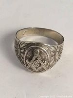 Front view of silver Freemasonry ring with square and compasses symbol and "G" in center