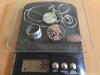 Photo showing 4 silver jewelry items (ring, two pendants, money clip) on scale reading 38g.