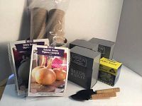 Front view showing seed packets including Spanish onions and white onions, biodegradable seed pots, small wooden-handled trowel and fork, and seed boxes.