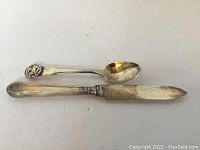 Two items displayed: a sterling silver collector spoon with Aries emblem and a vintage silver cutting utensil