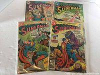 Four Superman comics, issues 307, 308, 310, 311, in protective plastic sleeves with visible front covers.