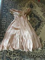 Full view of the pink vintage dress with off-shoulder neckline and floral detail on shoulder, laying on patterned carpet.