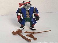 Panda Samurai action figure standing with three weapons (axe, sword, handgun) laid out in front showing colors and details