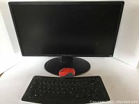 Full view of black computer monitor with curved base, red wireless mouse placed in front and black wireless keyboard below.