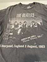 Front view of black cotton T-shirt featuring The Beatles in a 1963 Liverpool concert photo with text