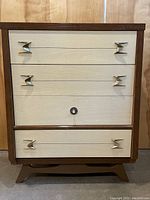 Full frontal view of the dresser showing light wood Formica drawers, dark solid wood frame, and brass atomic drawer pulls.