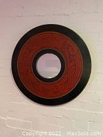 Front view of circular mirror mounted on a white brick wall showing black and reddish-brown hand carved frame and central mirror circle.