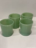 Top view of four pale green jadeite mugs arranged on white surface showing smooth interiors and round rims.