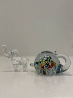 Side-by-side photo of clear glass smaller elephant and larger multicolor glass elephant