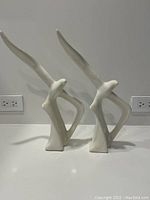 Pair of white stylized ceramic seagull sculptures with elongated wings, shown side by side on a countertop with power outlets in the background.