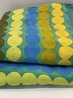 Close-up of folded sheet showing linked oval pattern in yellow, blue, and green colors on teal background fabric
