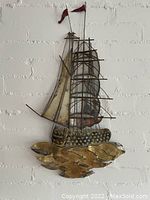 Frontal view of the brass sailing ship wall mounted decorative piece showing sails and brass base resembling waves.