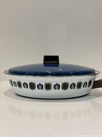 Side view of enamel skillet with lid on, showing peacock feather pattern around the body and long handle