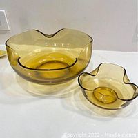 Two nesting amber yellow glass bowls with wavy rims on a flat surface