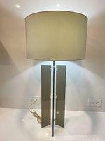 Front view of vintage lamp showing smoked acrylic X-shaped base and large off-white cylindrical shade.