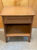 Full front view of the solid ash wood nightstand showing tabletop, drawer front, and open shelf below.