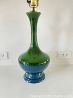 Another front angle view of lamp body on white table and white wall background, showing electrical cord coiled at base.