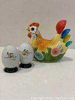 Front view of ceramic chicken spoon holder with colorful measuring spoons and paired ceramic egg salt and pepper shakers with farm animal illustrations.
