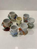 Seven vintage ceramic egg cups with various animal figurine bases arranged in a front-facing display