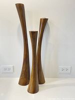 Three vintage mahogany candlesticks of varying heights shown upright together to display size and silhouette.