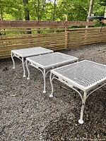 Three white wrought iron square tables side by side on gravel