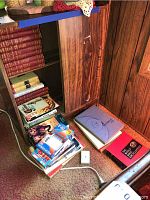 Shelf with hardcover yearbooks and encyclopedia volumes, a box of VHS tapes and DVDs stacked on the floor