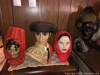 Four ceramic busts including one male and three female figures shown together on a doily on wood furniture surface
