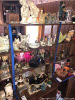 Shelf display of various figurines, vases, metal toy cars, a decorative kettle, candle holder, and other small decorative items.