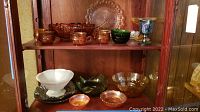 Full view of carnival glass collection on wood shelf showing variety of bowls, goblets, trays, including footed green glass bowls and amber glass items.