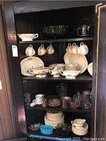 Full view of dark wooden shelves displaying various china items and glassware including plates, teacups, bowls, and pitchers.