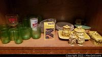 Shelf view with mushroom-themed dish set including shakers, creamer, sugar, tray, green glassware, dominoes, doll furniture