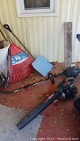 Full view of yard tools including snow shovel with blue dust pan, red rake, broom, pruners, weed whacker and leaf blower