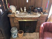 Fireplace mantel displaying figurines, candle holders, ceramic crock, teapot, candy dish and other items.